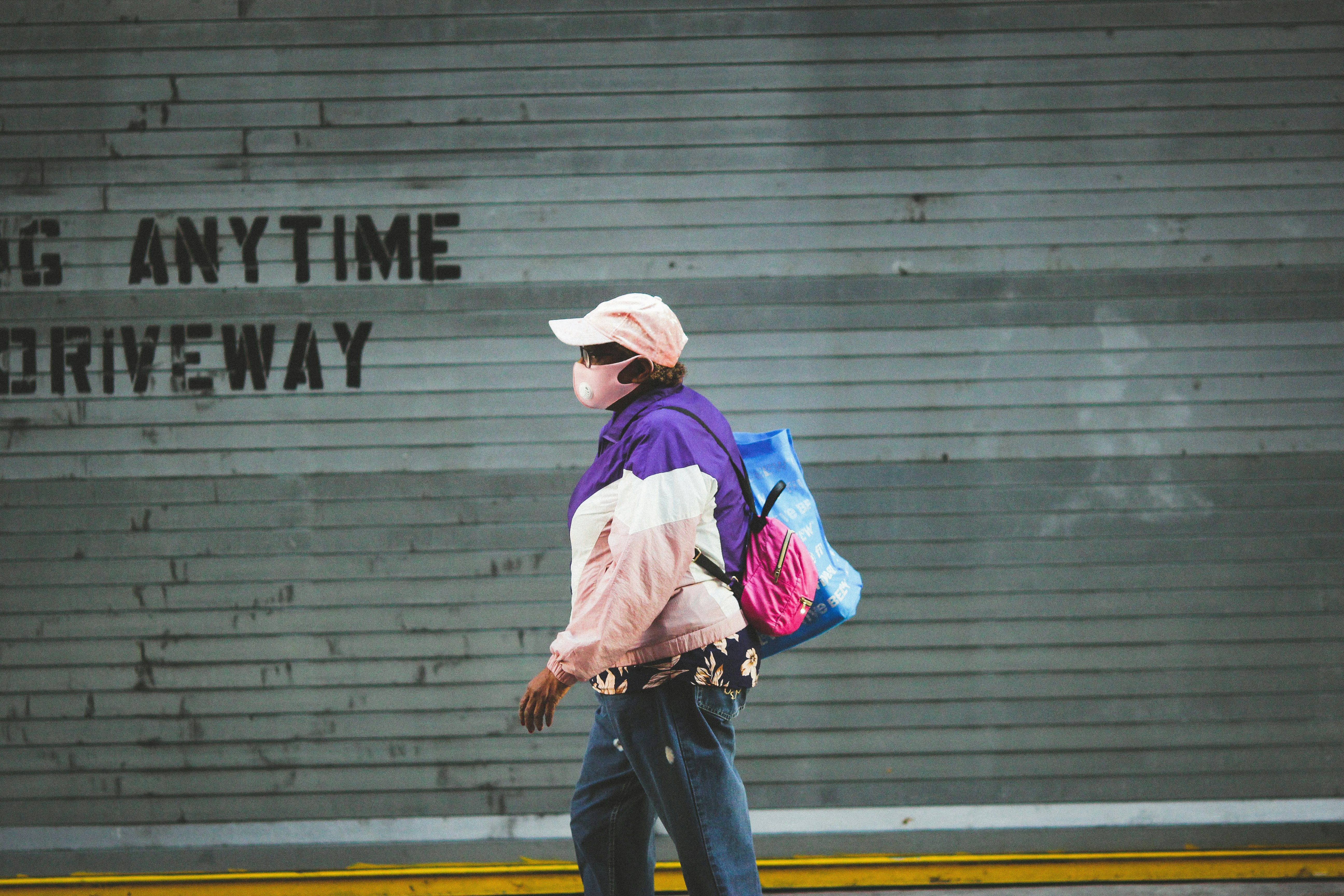 woman in pink hoodie and blue denim jeans standing near gray wall